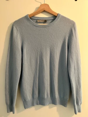 Ljusblå Cashmir Crewneck - En stilren ljusblå cashmir crewneck med rund halsringning och långa ärmar. Tröjan har ribbade muddar vid ärmslut och nederkant. Perfekt för lager på lager och enkel att matcha med olika outfits.