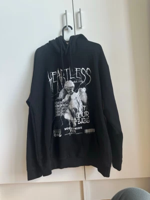Heartless hoodie - Heartless Hoodie från PrettyLittleThing med grafiskt tryck  Mindre missfärgning på ena axeln, syns knappt om man inte kollar noga (se bild)