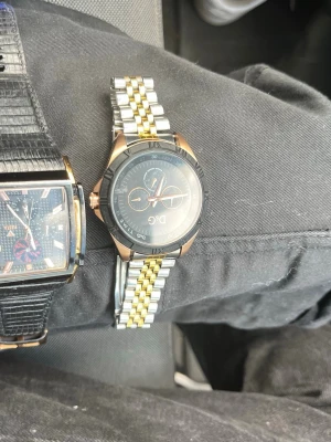 Två stilrena herrklockor - Säljer två snygga herrklockor. Den ena har svart och guldigt armband i metall och svart urtavla med detaljer i guld. Den andra har svart läderarmband med reptilmönster och rektangulär urtavla med guldiga detaljer. Perfekt för dig som vill ha klassiska accessoarer.