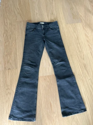 Mörkgrå bootcut jeans stö 152 Gina Tricot - Snygga mörkgrå bootcut jeans med klassisk femficksmodell och dubbla knappar i midjan. Jeansen har utsvängda ben och är tillverkade i ett mjukt denimtyg med stretch för extra komfort. 