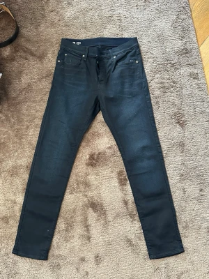 Mörkblåa G-Star Raw med stretch - Snygga mörkblåa jeans med fem fickor och smal passform. Jeansen har klassisk design med knappgylf och bälteshällor. Materialet är stretchigt för extra komfort och sitter tight hela vägen ner. Perfekta för en trendig och avslappnad stil.