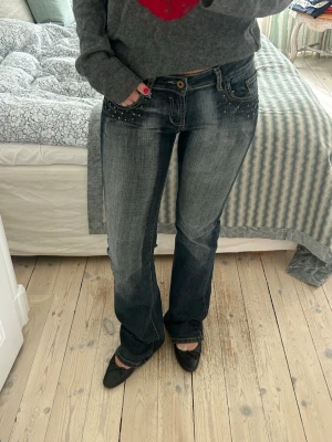 Bootcut jeans med nitar och slitningar - Snygga bootcut jeans i mörkblå tvätt med slitningar och coola nitar på fickorna fram och bak. Jeansen har låg midja och stora bakfickor med dekorativa detaljer. Står ingen storlek då jag köpte vintage men passar utmärkt på mig som har 34-36, det är väldigt töjbara så tror de funkar utmärkt om man har 38 också!