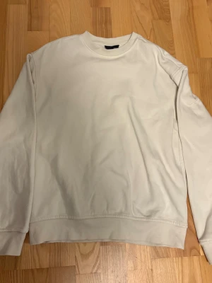 Vit basic sweatshirt - En stilren vit sweatshirt med rund hals och långa ärmar. Tröjan har ribbade muddar vid ärmslut och nederkant. Perfekt för en enkel och clean look, lätt att matcha med olika outfits.