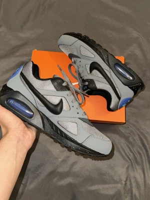 Nike grå och svarta sneakers 👟 -  Säljer ett par stilrena Nike Air Max Torch 4 i en snygg grå/svart färgkombination med blå detaljer.  Skorna är helt oanvända och i nyskick. De har aldrig använts utomhus och kommer med originalkartong. Perfekta för dig som söker ett par bekväma och stilrena sneakers som passar både till vardags och en sportigare outfit.  Detaljer:  * Modell: Nike Air Max Torch 4 * Färg: Grå / svart med blå detaljer * Skick: Oanvända / nyskick * storlek 42
