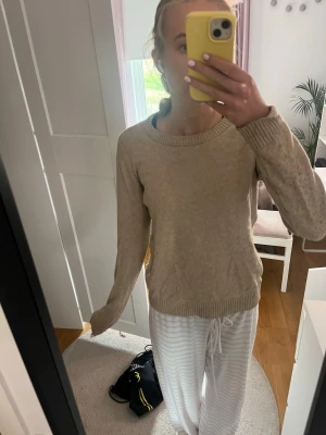 Beige stickad tröja med rund hals - En enkel och stilren beige stickad tröja med rund halsringning och ribbade muddar vid ärmslut och nederkant. Perfekt basplagg till garderoben och lätt att matcha med olika outfits. Tröjan har en rak passform och långa ärmar.