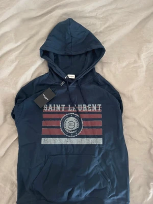  Saint Laurent hoodie - Säljer en riktigt snygg och hoodie från Saint Laurent i navy. Den är bara använd en gång och är i storleken M. Sitter perfekt på ca 185