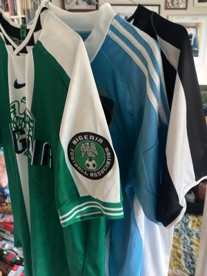 3 tröjor - Säljer en klassisk Nigeria fotbollströja från Nike i grönt och vitt med emblem från Nigeria Football Association på ärmen. Tröjan har korta ärmar, rund hals och sportig design, perfekt för fotboll eller träning.