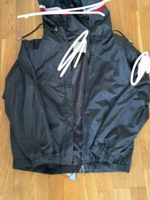 M windbreaker   - Moncler windbreaker  Aldrig använd storlek M  Väldigt skön och fräsch inför hösten.  Med trycket på armen och den slingrande röd vita färgen runt huvudet sticker man ut från mängden. Väldigt efterfrågad  Skickar samma dag eller dagen efter 