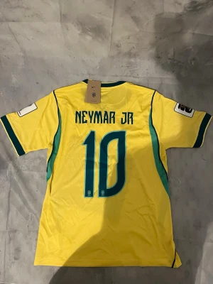 Gul Brasil Neymar fotbollströja - Säljer en gul Brasilien fotbollströja från Nike med Neymar Jr och nummer 10 på ryggen. Tröjan har gröna detaljer, officiella CBF-loggan på bröstet och korta ärmar. Perfekt för dig som älskar fotboll och vill stötta Brasilien.