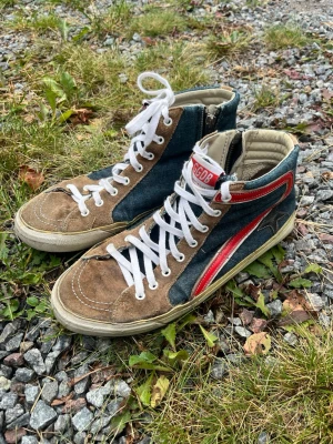 Golden Goose sneakers - Riktigt snygga Golden Goose Deluxe Brand high-top sneakers, Made in Italy. En äldre modell med mörkblå denim, bruna mockadetaljer, röda läderdetaljer och den klassiska stjärnan på sidan. Dragkedja på insidan gör dem enkla att ta av och på. Skorna är väl använda och i behov av kärlek/reparation, framför allt har sulan släppt på flera ställen och behöver limmas eller lämnas in till skomakare. Se bilder för skick. Hälen är däremot nyligen lagad/omsulad, så där finns nytt material. 