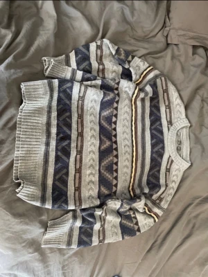Gråblå mönstrad grandpa sweater tröja - Säljer en stickad tröja i grått och blått med geometriskt mönster och inslag av beige och vinrött. Perfekt för dig som gillar retrovibbar och sköna material. Okänd storlek men skulle tippa M/L. Köpt i London för 500