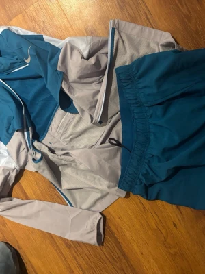Nike Miller  - Säljer ett par blå sportiga shorts från Nike med klassisk logga på vänster ben. Shortsen har en avslappnad passform och elastisk midja, perfekta för träning eller chill. Materialet känns lätt och andas bra, vilket gör dem grymma för varma dagar. Jackan och shorts tillkommer