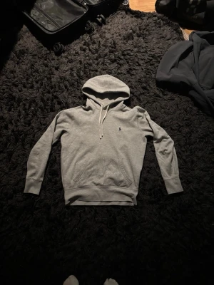 Grå hoodie från Polo Ralph Lauren XS - Snygg grå hoodie från Polo Ralph Lauren i storlek XS. Klassisk design med huva och dragsko, samt liten broderad logga på bröstet. Mjuk bomullsblandning och känguruficka framtill. Perfekt för en chill och stilren look.