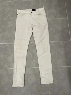 Vita slim jeans tiger of Sweden - Snygga vita slim jeans med klassisk femficksdesign och smal passform. Jeansen har normal midja och stängs med knapp och dragkedja. Perfekta för dig som vill ha en clean och stilren look. Modellen heter evolve