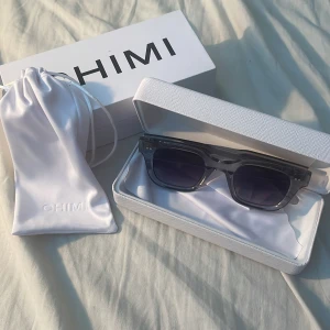 Grå transparenta solglasögon från CHIMI 04 - Snygga solglasögon från CHIMI med transparent grå båge och mörka glas. Rektangulär form som ger en modern look. Kommer med vit hård förvaringsbox och tygpåse med CHIMI-logga. Skulle säga att dom är 9/10.
