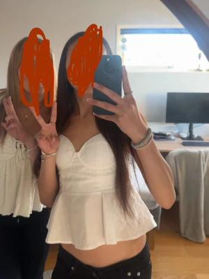 Vit ärmlös peplumtop - Säljer en söt vit ärmlös peplumtop med hjärtformad urringning och figurnära passform upptill. Toppen har en volang nedtill som ger en feminin siluett. Perfekt att styla med jeans eller kjol för en trendig look. Endast använd 1 gång, säljer då den inte kommer till användning.