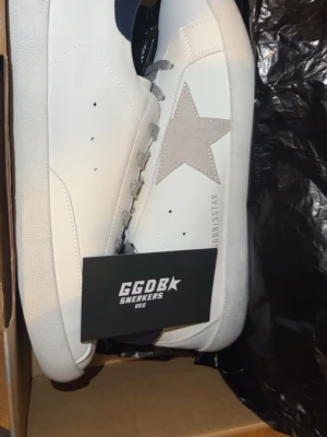 Golden Goose  - Snygga vita sneakers från Golden Goose med grå stjärna på sidan, grå skosnören och mörkblå detalj vid hälen. Klassisk låg modell i läder med perforerade detaljer på tungan. Perfekta för dig som gillar stilrena och trendiga skor.Storlek 44 men passar 43 också , 27,5 är solen.