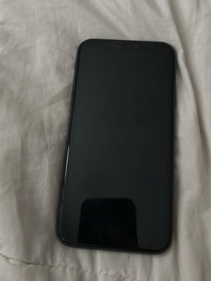 Svart iPhone 11 med dubbla kameror - Säljer en svart iPhone 11 med stilren design och rundade kanter. Telefonen har dubbla bakre kameror och en glasbaksida med Apple-loggan. Perfekt för dig som gillar snygg och modern teknik.