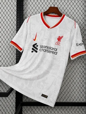 Vit Liverpool fotbollströja - Snygg vit Liverpool fotbollströja med röda och gula detaljer på krage och ärmslut. Tröjan har klubbmärke och sponsorloggor framtill samt tryck på ärmen. Tillverkad i lätt och ventilerande material, perfekt för träning eller match.
