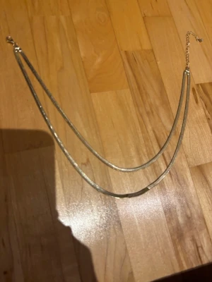Dubbel kedjehalsband i guldton - Snyggt halsband med två tunna, platta kedjor i guldton. Halsbandet har en justerbar kedja med lås och ger en stilren och trendig look. Perfekt för att lyfta vilken outfit som helst med en enkel men elegant touch.