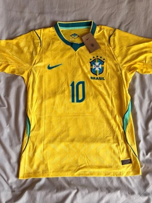 Brasilien Neymar JR matchtröja gul - Säljer en officiell Brasilien matchtröja från Nike i gult med gröna detaljer. Tröjan har nummer 10 och Neymar JR tryckt på ryggen samt CBF-emblemet på bröstet. Tillverkad i lätt och ventilerande material, perfekt för fotboll eller träning.