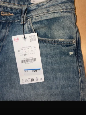 Blå raka jeans med slitningar - Säljer ett par blå jeans med raka ben och trendiga slitningar på både fram- och baksida. Jeansen har klassisk femficksmodell och normal midja. Perfekta för en avslappnad och cool stil. Materialet är denim i bomull.