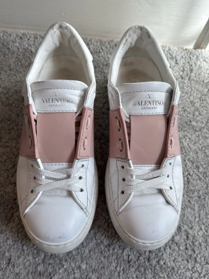 Valentino Open rosa💗 - Snygga vita sneakers från Valentino Garavani med ljusrosa detaljer. Skorna har klassisk låg modell, vita snören och nitar på hälen. Dessa är tidigare köpt från plick men varit för småa för mig!💗Ett fint skick och sparsamt använda! obs!! Låda, tygpåse och tillbehör tillkommer med ditt köp! Skriv för mer bilder eller frågor!💗