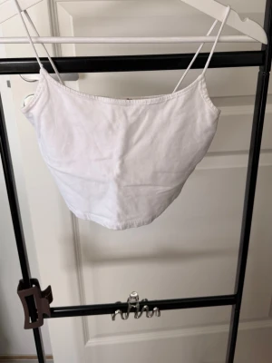 Vit croppad linnetopp - Säljer en enkel och stilren vit croppad linnetopp med tunna axelband. Perfekt till sommaren och lätt att matcha med olika outfits. Toppen har en rak passform och är tillverkad i mjukt bomullstyg.
