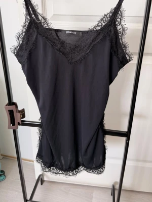 Svart spetsnattlinne från Gina Tricot - Snyggt svart nattlinne från Gina Tricot med tunna axelband och dekorativ spets längs urringning, nederkant och sidor. Mjuk och följsam känsla, perfekt för mysiga kvällar hemma. Enkel och elegant design som känns både klassisk och trendig.