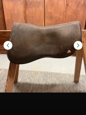 Brun sadelpadd från Acavallo - En brun sadelpadd i filtmaterial med ergonomisk form, perfekt för att lägga under sadeln vid ridning. Den har en diskret design utan synliga mönster och passar bra till olika sadlar. Enkel att använda och ger extra komfort till hästen.