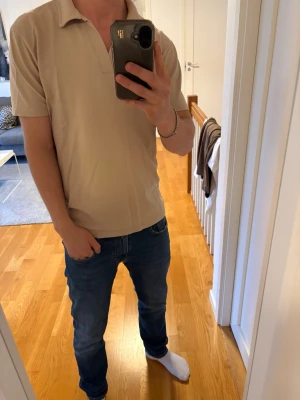 Beige pikétröja med krage - Snygg beige pikétröja med klassisk krage och kort ärm. Tröjan har en avslappnad passform och är tillverkad i ett mjukt material som känns skönt mot huden. Perfekt för en stilren och enkel look.
