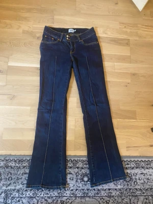 Mörkblå bootcut jeans med söm - Snygga mörkblå bootcut jeans med markerad mittsöm framtill. Klassisk femficksmodell med kontrastsömmar och hög midja. Jeansen har en lätt utsvängd passform nedtill och är tillverkade i denim med stretch för extra komfort.