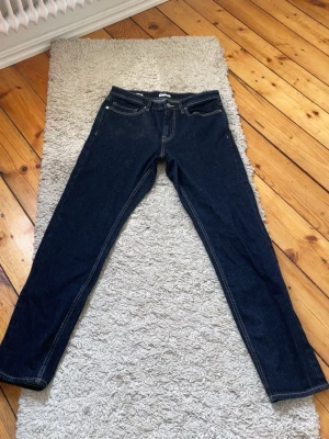 Mörkblå raka jeans 31/32 - Säljer ett par mörkblå jeans med raka ben och klassisk femficksmodell. Jeansen har kontrastsömmar och silverfärgad knapp. Perfekta till en avslappnad stil och tillverkade i slitstarkt denimtyg. Ord pris 499