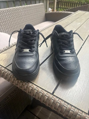 Svarta låga sneakers i läder - Snygga helsvarta sneakers i lågt modell med klassisk siluett och perforerad tåbox. Skorna har svarta skosnören och diskreta detaljer, tillverkade i läder för en clean look. Perfekta för dig som gillar stilrena och tidlösa sneakers.