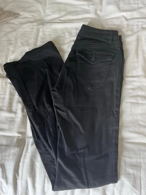 Svarta skinny jeans med fickdetalj - Säljer ett par svarta skinny jeans med hög midja och snygg fickdetalj bak. Jeansen har klassisk femficksmodell och knappgylf. Materialet är stretchigt för en bekväm passform och de passar perfekt till en trendig vardagslook.