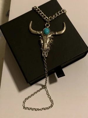 Armband med tjurhuvud och turkos sten - Unikt armband i silverfärgad metall med ett detaljerat tjurhuvud som hänge. I mitten sitter en rund turkos sten. Kedjan är grov och har en extra kedja som hänger ner. Perfekt för dig som gillar boho eller westernstil.