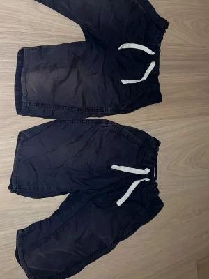 Marinblåa shorts med snörning - Två par mörkblå shorts med vita snören i midjan, bakfickor och även så man kan spänna in de i midjan. Båda är i storlek 152.