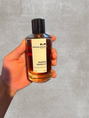 Mancera Roses Vanille EdP 120ml - Mancera Roses Vanille Eau de Parfum i en elegant cylinderformad glasflaska med svart metallock. Doften har en varm bärnstensfärgad vätska och etiketten är stilren i vitt och svart. Flaskan rymmer 120 ml och har exklusiv känsla.
