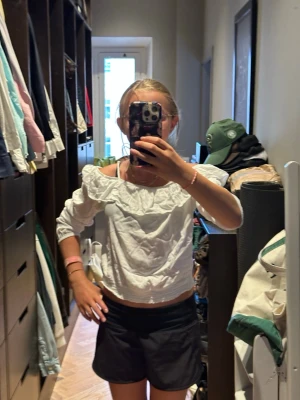 Vit offshoulder blus med volang - Säljer en söt vit offshoulder blus med volangdetalj längs ringningen. Blusen har långa ärmar och smockad nederkant som ger en snygg passform. Perfekt till sommaren och lätt att matcha med både jeans och kjol.
