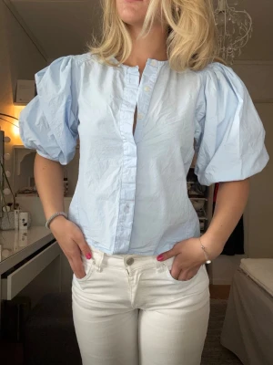 Ljusblå blus med puffärm - Trendig ljusblå blus med puffiga korta ärmar och har knappar framtill. Perfekt som en brunch blus!