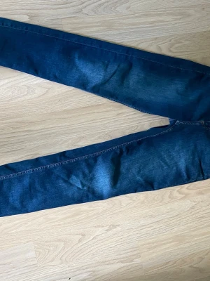Mörkblå skinny jeans - Säljer ett par mörkblå skinny jeans med klassisk femficksdesign och lätt slitningar på låren. Jeansen har normal midja och smala ben, perfekta till en avslappnad stil. Materialet är troligtvis bomull med lite stretch för extra komfort.