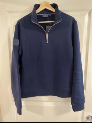 Marinblå halfzip hoodie Race Marine - Marinblå hoodie från Race Marine med halv dragkedja och hög krage. Tillverkad i mjukt material, långärmad och ribbade muddar vid ärmslut och nederkant. Enkel och stilren design utan tryck eller mönster, perfekt för en clean look.