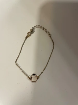 Sött armband med pingvinberlock - Armband i silverfärgad metall med en liten pingvinberlock i vitt och svart emalj. Kedjan är tunn och har ett klassiskt lås. Perfekt för dig som gillar gulliga detaljer och djurmotiv.