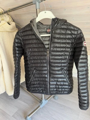 Colmar jacka  - Snygg svart Colmar jacka med huva och dragkedja framtill. Jackan har två fickor med dragkedja och quiltad design. Perfekt för kalla vinterdagar och riktigt lätt att bära.