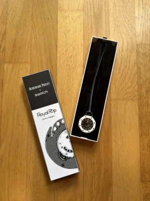 Swatch x Audemars Piguet Royal Pop klocka - Säljer en Swatch x Audemars Piguet Royal Pop Ocho Negro klocka med svart urtavla och vit ram. Klockan har en modern, oktagonal form och svart band. Snygg och unik accessoar för dig som gillar stilrena detaljer.