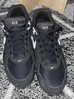 Nike Air Max svartvita sneakers - Snygga Nike Air Max sneakers i svart och vitt med klassisk logga på sidan och meshdetaljer på ovandelen. Skorna har lågt skaft, svarta skosnören och en bekväm sula som ger bra dämpning. Perfekta för dig som gillar streetwear och sportig stil.