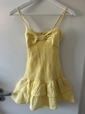 Gul klänning 💛💛 - Superfin gul klänning från design by amor i storlek xs, perfekt till sommaren! 💕💕Klänningen har smala, justerbara axelband, en stor rosett framtill, smockad överdel för en bekväm och smickrande passform samt ett sött gulvitt rutigt mönster med volangdetaljer. Den är helt oanvänd och har prislappen kvar. Säljer då den tyvärr inte passade mig.  