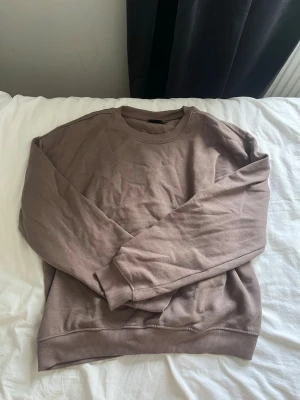 Brunt loungewear-set i bomull - Mysigt loungewear-set i mjuk bomull med en brun sweatshirt och matchande byxor med resår i midjan och dragsko. Perfekt för chill dagar hemma eller när du vill vara bekväm. Båda plaggen har avslappnad passform och ribbade muddar.