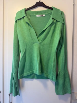 Grön stickad tröja från Adoore - Trendig grön stickad tröja från Adoore med djup v-ringning, stor krage och vida ärmslut. Perfekt för dig som vill sticka ut med en färgglad och snygg look. Materialet är mjukt och följsamt, vilket gör den superbekväm att bära.