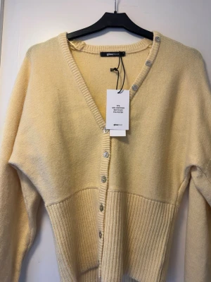 Gul kofta från Gina Tricot - Snygg gul kofta från Gina Tricot med v-ringning och knappar framtill. Koftan har ribbstickad nederdel och muddar, samt långa ärmar. Tillverkad i en mjuk materialmix med polyester och återvunnen polyester. Perfekt för lager på lager och enkel att styla.